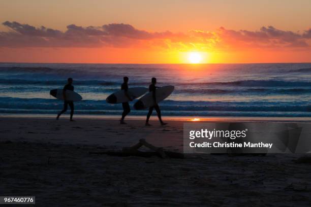 morning surfers walking along beach ready to catch the waves in the sunrise - ireland surf wave stockfoto's en -beelden