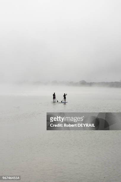 Des vacanciers pratiquent le paddle sur l'étang de Péroles embrumé par les entrées maritimes, 29 juin 2016, Hérault, France.