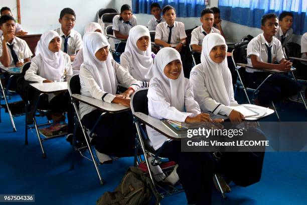 Intérieur d?une classe où lycéens et lycéennes musulmans, vêtus de l?uniforme scolaire indonésien exigeant le port du voile par les filles, suivent...