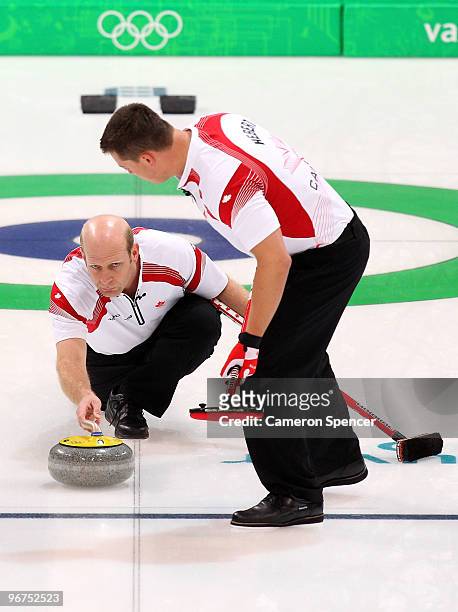 Skip Kevin Martin of Canada releases his stone as teammate Benjamin Hebert looks on during the men's curling round robin game between Canada and...