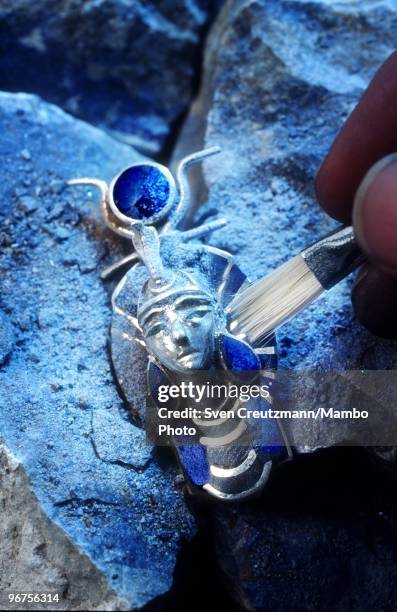 Model brushes off dust from a jewellery Tutankhamen death mask made of the precious stone Lapis Lazuli, atop a raw Lapis Lazuli stone in the Flores...