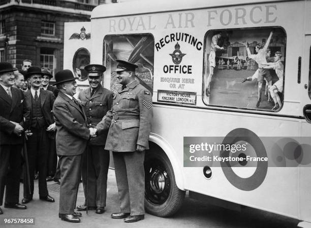 Le secrétaire d'Etat à l'Air, Sir Kingsley Wood serre la main du sergent recruteur devant le bureau mobile de recrutement de l'armée positionné à...