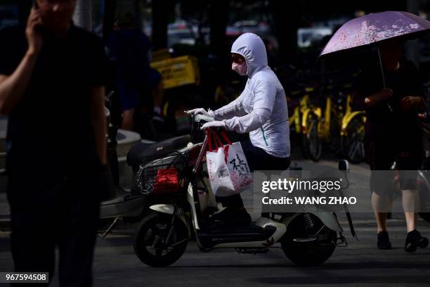 Woman wearing sun-proof clothing commutes along a street in Beijing on June 5, 2018. - The Beijing weather department issued a yellow warning signal...