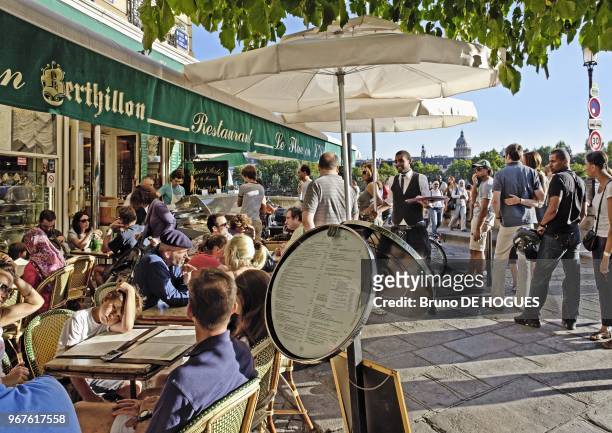 Some people on cafe terrace and some other people waiting to buy Berthillon ice creams at Le Flore restaurant in St Louis Isalnd on July 18, 2010 in...