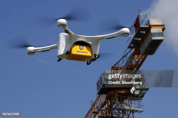 Construction crane stands beyond as an M2 delivery drone, manufactured by Matternet Inc., carries a Swiss Post International Holding AG branded box...