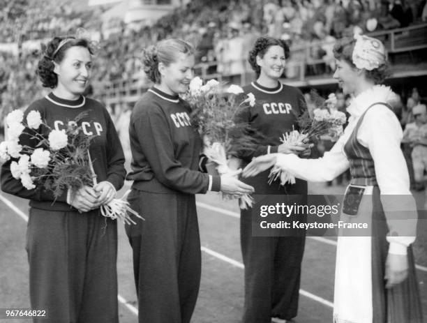 Une jeune Finlandaise en costume traditionnel remet des bouquets de fleurs aux trois femmes soviétiques qui ont remporté l'épreuve olympique du...