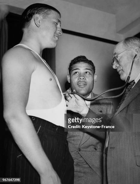 Le champion du monde poids lourds, Joe Louis, regarde son adversaire Tommy Farr se faire examiner par le médecin de la commission de boxe, à New York...