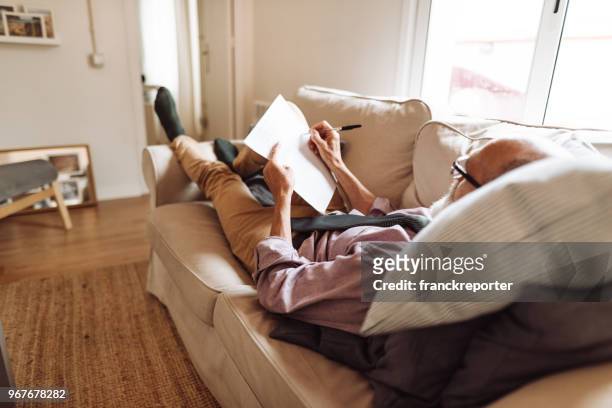 senior man writing a document lying down in the sofa - writing a list stock pictures, royalty-free photos & images