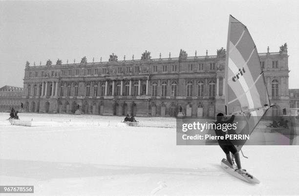 Jean-Pierre Mercier sur un bassin gelé du parc de Versailles fait de la planche à voile par un froid glacial le 14 janvier 1985, France.