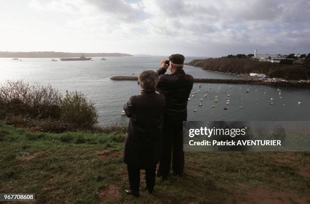 Un couple observe à la jumelle le porte-avions à propulsion nucléaire 'Charles de Gaulle' lors de sa première sortie le 26 janvier 1999 à Brest,...