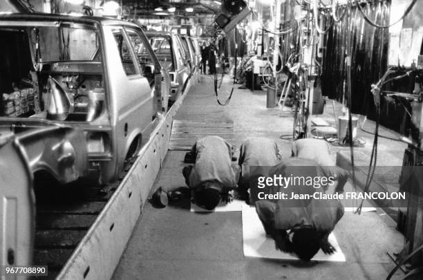 Des ouvriers musulmans font leur prière à genoux dans l'atelier près de la chaîne de montage des voitures dans une usine Talbot le 18 juillet 1983 à...