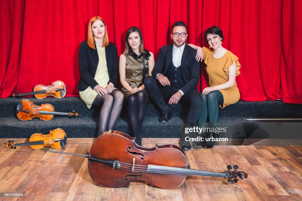 String quartet posing after the concert with their instruments on stage.