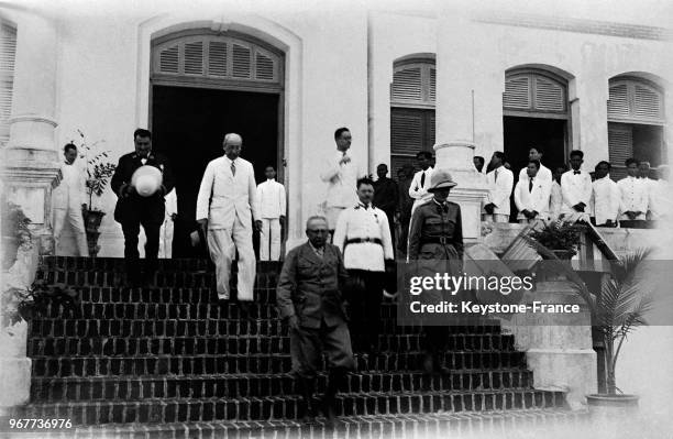 René Robin, gouverneur général de l'Indochine, descend le perron de la résidence de la région de Kompong-Thom, derrière lui en costume civil blanc,...