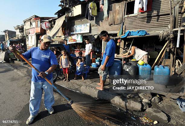 Streetsweeper cleans a curb along a crowded roadside shantytown in downtown Manila on February 17, 2010. Twenty-one million Asians could fall back...