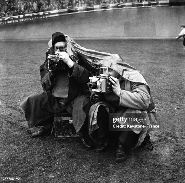 Des photographes accroupis sur le bord du terrain suivent le match protégés par un imperméable, à Paris, France le 29 janvier 1956.