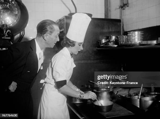 Yvonne Printemps en tenue de cuisinière préparant un plat pour son camarade René Koval, à l'occasion d'un déjeuner organisé pour la société sportive...