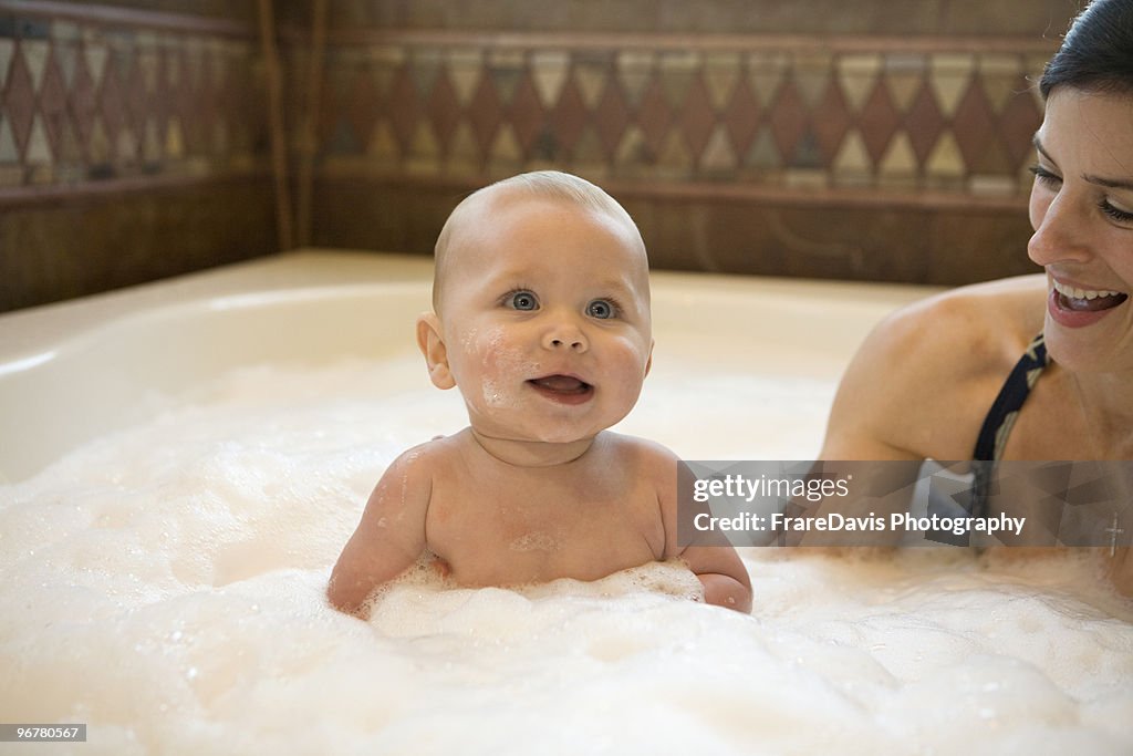 Baby smiles in bubble bath with mother.