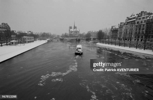 Vue de la cathédrale Notre-Dame, de la Seine avec une péniche et des quais enneigés le 14 décembre 1987 à Paris, France.