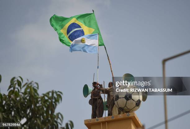 This picture taken on June 5 shows two Pakistani soccer fans fixing the flags of Argentina and Brazil at a house's roof ahead of the FIFA World Cup...