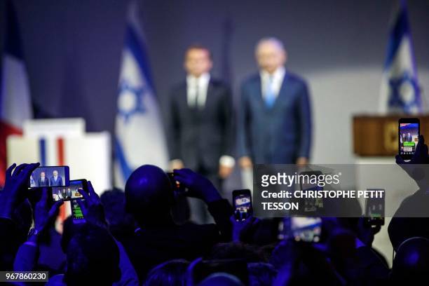 Peopole from the audience take pictures with their mobile phones of French President Emmanuel Macron and Israeli Prime Minister Benjamin Netanyahu...