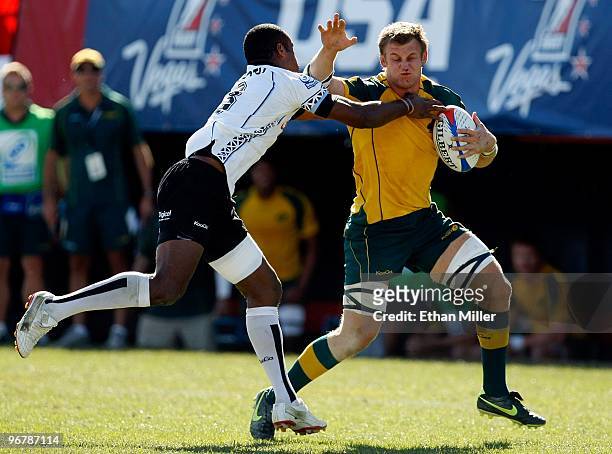 Pat McCutcheon of Australia bleeds from his nose as he avoids a tackle by Watisoni Votu of Fiji en route to scoring a try during the IRB Sevens World...
