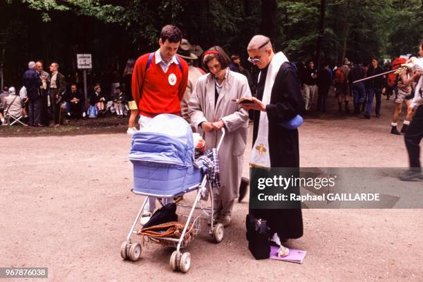 Prêtre auprès d'un couple et de son enfant lors du traditionnel pèlerinage de Pentecôte entre Paris et Chartres le 15 mai 1989, France.