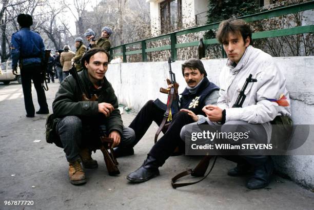 Trois combattants, fusil-mitrailleur en main, se reposent derrière un muret, à Bucarest, Roumanie le 24 décembre 1989.