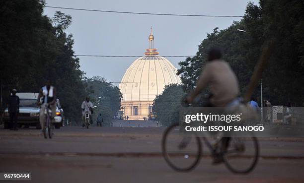 The dome of the "Notre Dame de la Paix" basilica is seen in the background as a man rides a bicycle in the streets of Yamoussoukro, the...