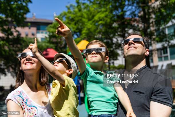 family looking at solar eclipse in the city street in a public park - solar eclipse glasses stock pictures, royalty-free photos & images