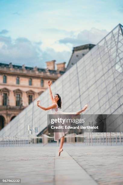 Ballet dancer Amanda Derhy performs an "Attitude", wears a white leotard, repetto ballerina shoes and a light purple skirt, in front of the Louvre...