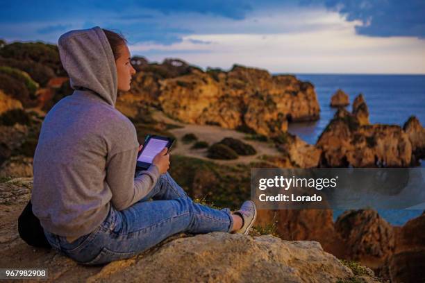 年輕的黑髮女性閱讀她的電子閱讀器在 alvor 葡萄牙的懸崖在夏末的太陽 - e reader 個照片及圖片檔