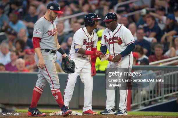 Ozzie Albies and first base coach Eric Young of the Atlanta Braves react after Albies reached safe on an error by the Washington Nationals at...