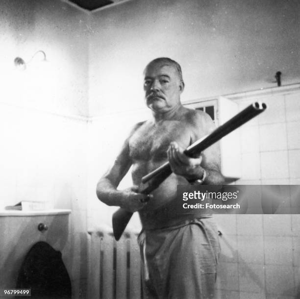 Ernest Hemingway standing with shot-gun indoors circa 1950s. .