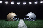 Football helmets facing off on a yard line under stadium lights at night