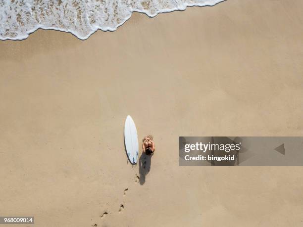 young surfer woman sitting on the sand beach with footprints on sand - beach footprints stock pictures, royalty-free photos & images