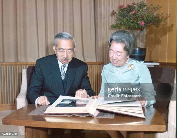 Emperor Hirohito and wife Empress Kojun sit looking over family photo album, circa 1950s. .