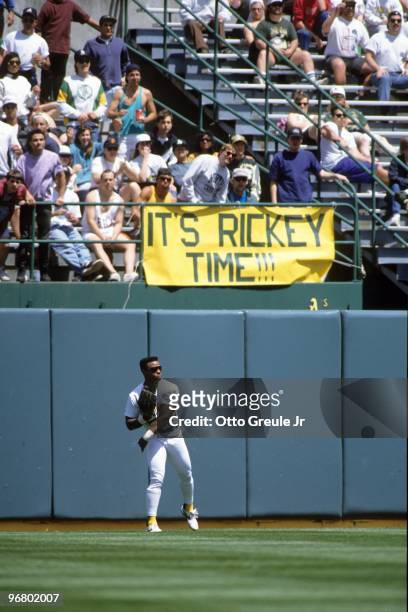 Rickey Henderson of the Oakland Athletics stands near the warning track in the outfield as fans display a sign during their MLB game against the New...