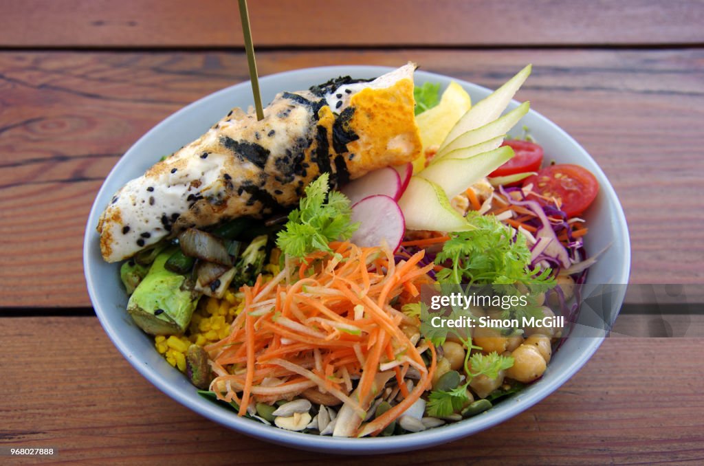 Buddha bowl with salad, pear, cherry tomato, red cabbage, broccoli, charred greens, chickpeas, grated carrot, sprouts, rice, grains, nuts, seeds & lemon hummus topped with a seaweed & black sesame omelette