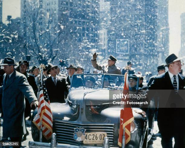 General Douglas MacArthur riding in an open car waving to well wishers, April 20, 1951. .