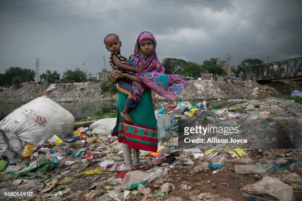 Girl holds a baby outside a plastic factory situated along a canal that leads to the Buriganga river on June 3, 2018 in Dhaka, Bangladesh. Bangladesh...