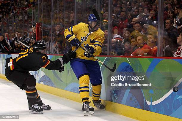 Henrik Tallinder of Sweden is checked against the boards by John Tripp of Germany during the ice hockey men's preliminary game on day 6 of the...