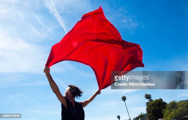 hip man holding onto red fabric flag against blue sky - red scarf stock-fotos und bilder