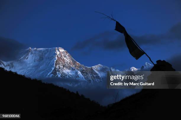 a buddhist prayer flag silhouetted against a backdrop of snow covered mountains at dusk, manaslu circuit trek, nepal - annapurna circuit photos et images de collection