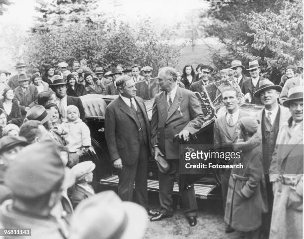 President Franklin D. Roosevelt standing outdoors near an open car with a crowd of people nearby, circa 1940s. .