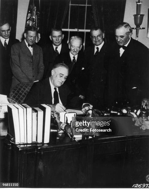 President Franklin D. Roosevelt seated surrounded by colleagues signing documents , circa 1940s. .