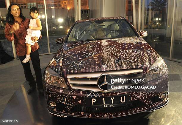 Popular Indonesian musician Satriyo "Piyu" Yudi Wahono holds his daughter Mikaela as he stands next to his Mercedes-Benz C 250 Batik version during a...