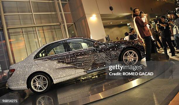 Popular Indonesian musician Satriyo "Piyu" Yudi Wahono holds his daughter Mikaela as he stands next to his Mercedes-Benz C 250 Batik version during a...