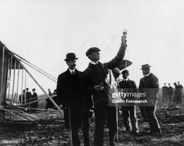 Picture of the Wright Brothers with Orville watching Wilbur take readings outdoors, circa 1908. .