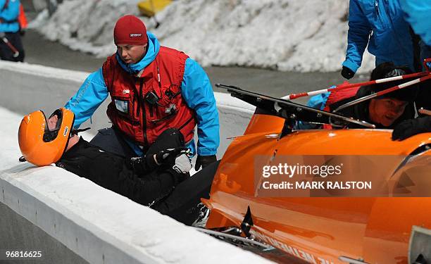 Members of the Dutch team led by pilot Edwin van Calker are helped by staff after crashing during the first training heat of the men's two-man...
