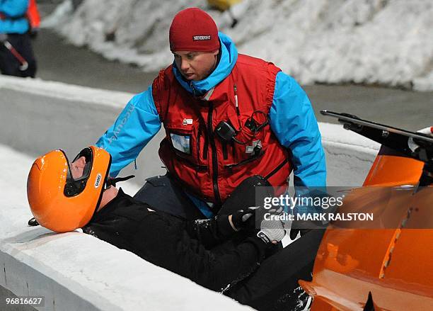 Members of the Dutch team led by pilot Edwin van Calker are helped by staff after crashing during the first training heat of the men's two-man...